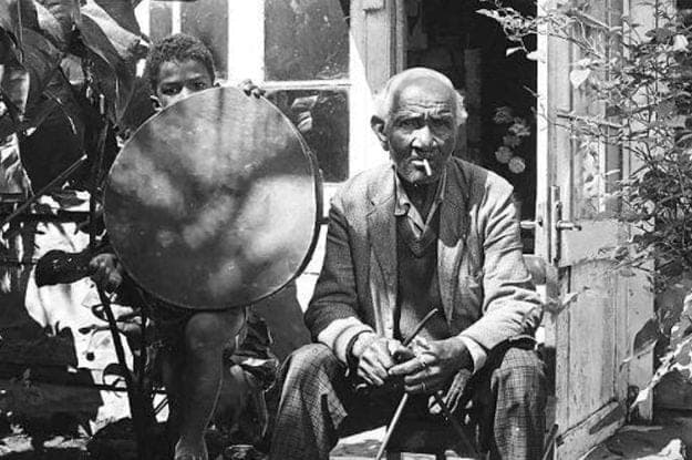 Ti Frère seated outside beside a young ravanne player