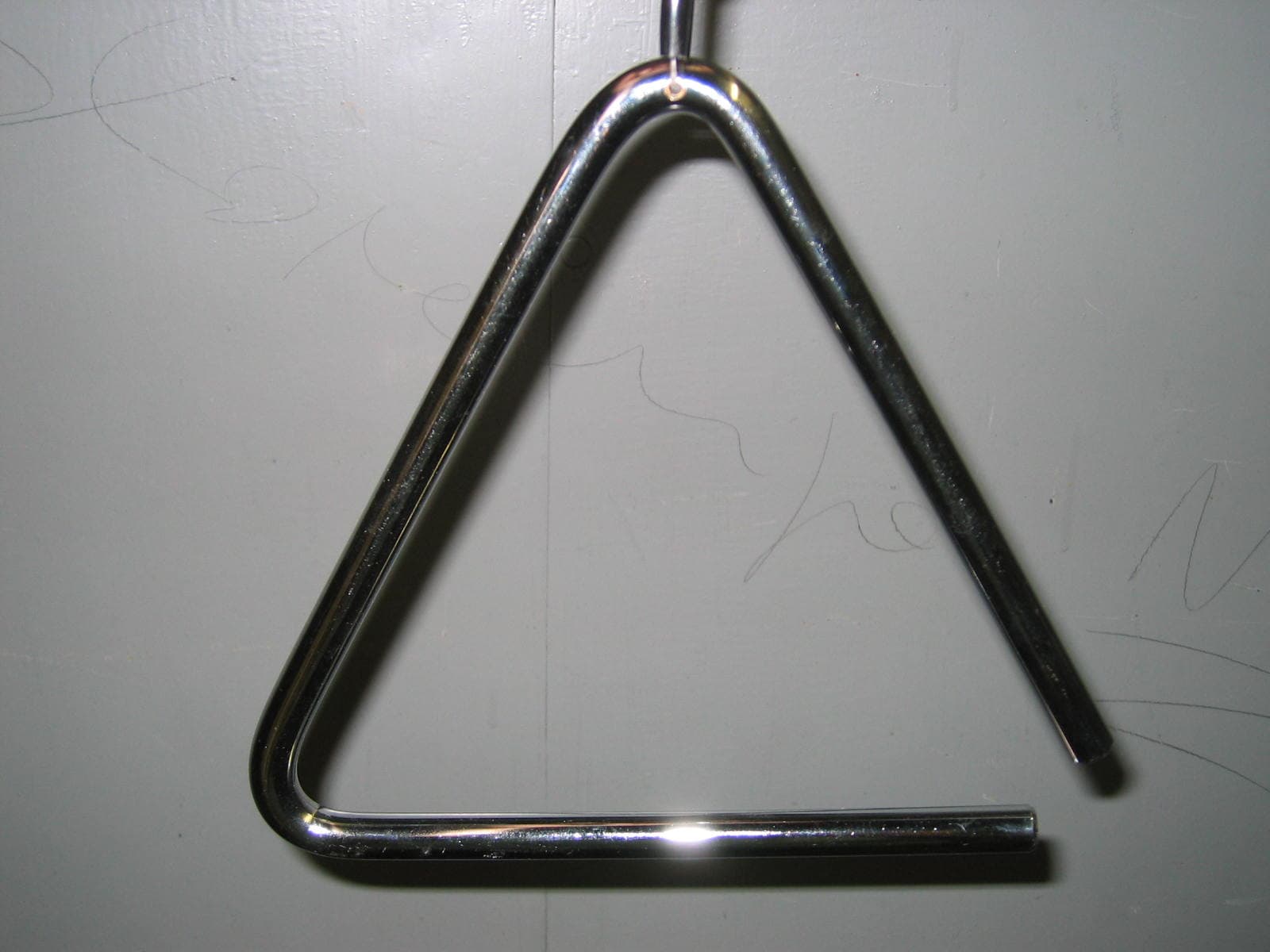 Metal triangle percussion instrument suspended against a pale surface